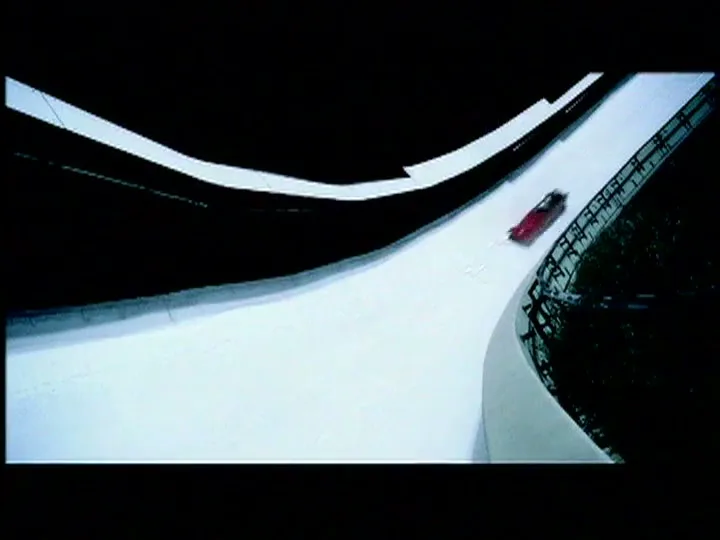A red bobsled speeds down a snowy track, viewed from above as it rounds a curve.