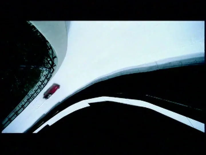 A red bobsled speeds down a snowy track, viewed from an overhead perspective, with dark shadows contrasting the white snow.