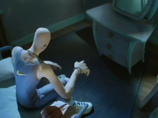 A claymation figure with a Nike tank top sits on the floor next to a bed, putting on a bracelet in a dimly lit room.