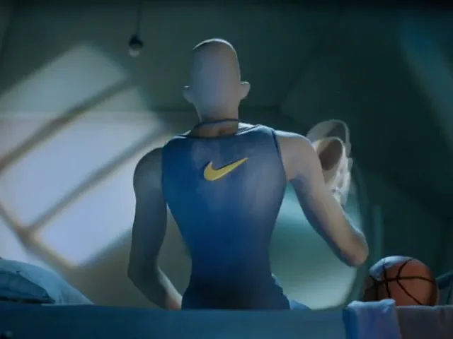 A bald, animated male character in a blue tank top with a Nike logo sits on a bed, holding a basketball shoe in a dimly lit room.