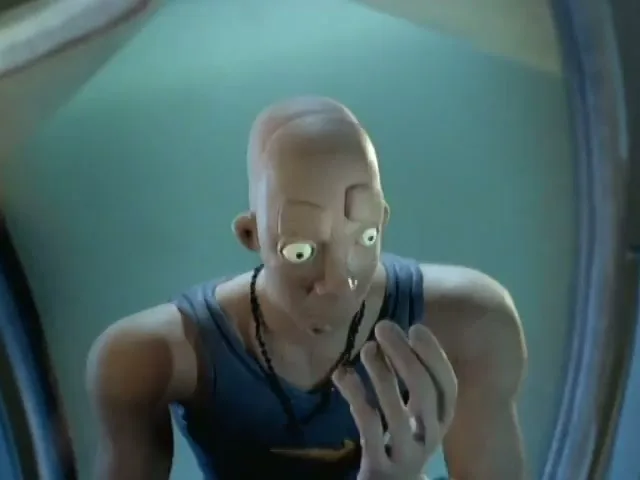 A bald, animated male character in a blue tank top looks at his reflection in a mirror, touching his face as his features appear.