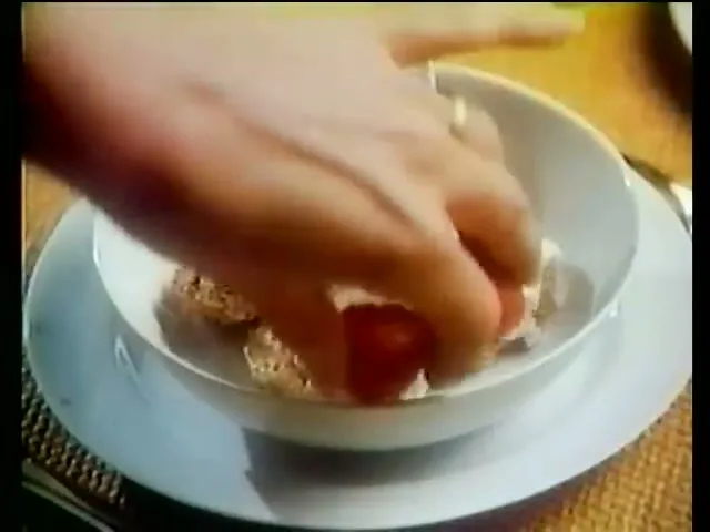 A female hand adds strawberries to a bowl of Weetabix cereal, then milk is poured over it, on a breakfast table.