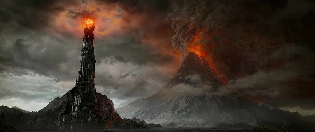 A dark, mountainous volcanic landscape dominated by a massive erupting volcano and a tower. The tower features a glowing, flaming eye at its peak under a thick storm cloud.