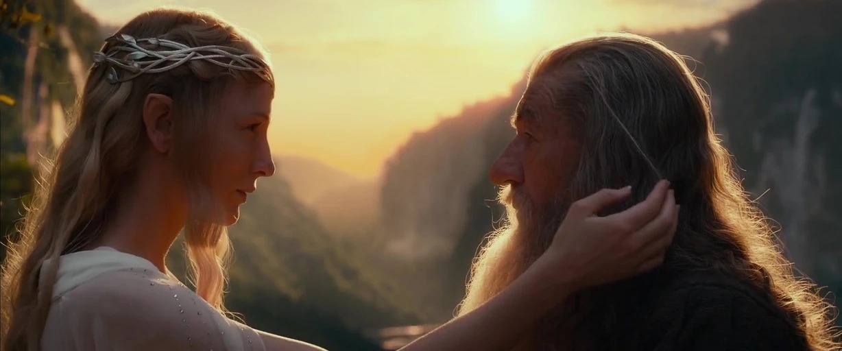 A high mountain terrace overlooking a valley during a vibrant, golden sunset. A woman with pointed ears gently brushes the long hair of a bearded man.