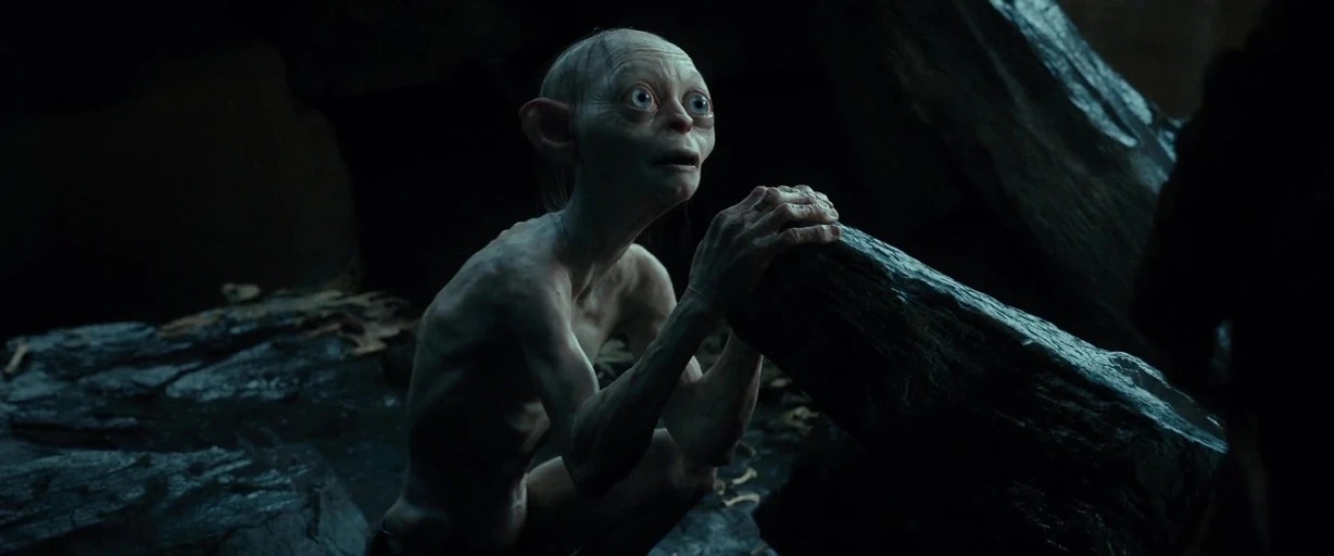 A dark rocky cavern with uneven surfaces and minimal light penetration in the background. A thin pale creature crouches on a jagged stone ledge staring toward the light.