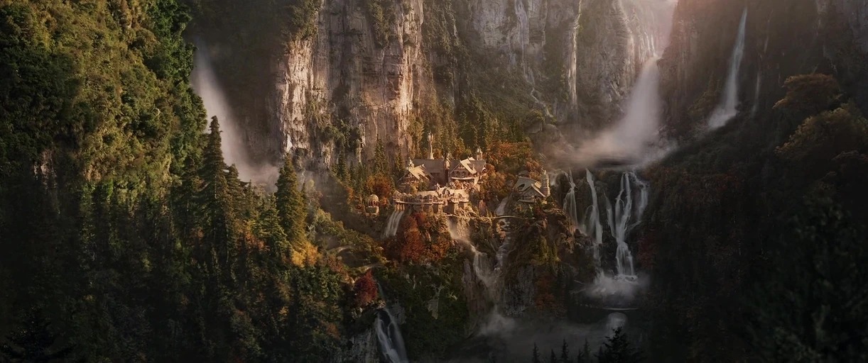 A sprawling valley nestled between steep rock cliffs contains a village with ornate structures. Multiple waterfalls cascade from the heights into a dense, misty, temperate evergreen forest floor.