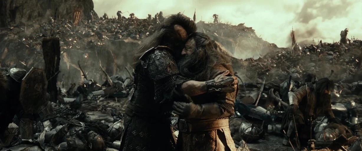 A war-torn rocky landscape filled with fallen debris and scattered weapons of combatants. Two armored men embrace with their foreheads touching amidst the aftermath of conflict.