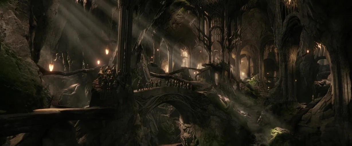 A sprawling subterranean hall carved from rock features tall arched pillars and winding stone bridges. Lines of people walk along the bridges through the dimly lit, moss-covered cavernous expanse.