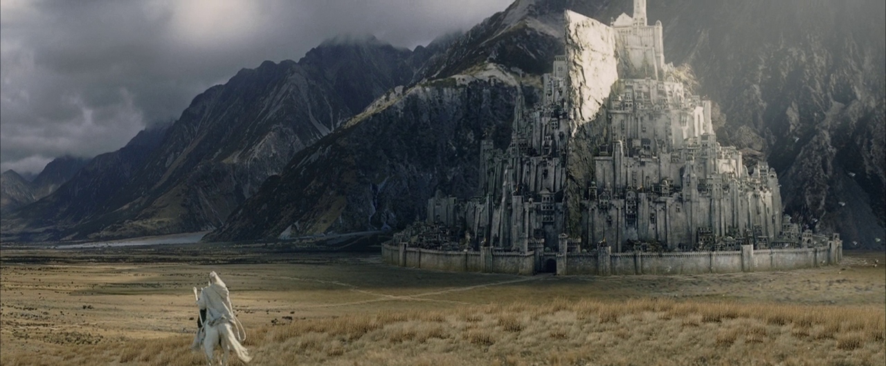 A vast valley landscape features a sprawling white fortified city built against mountains. A lone figure on a white horse travels across the grassy plains.