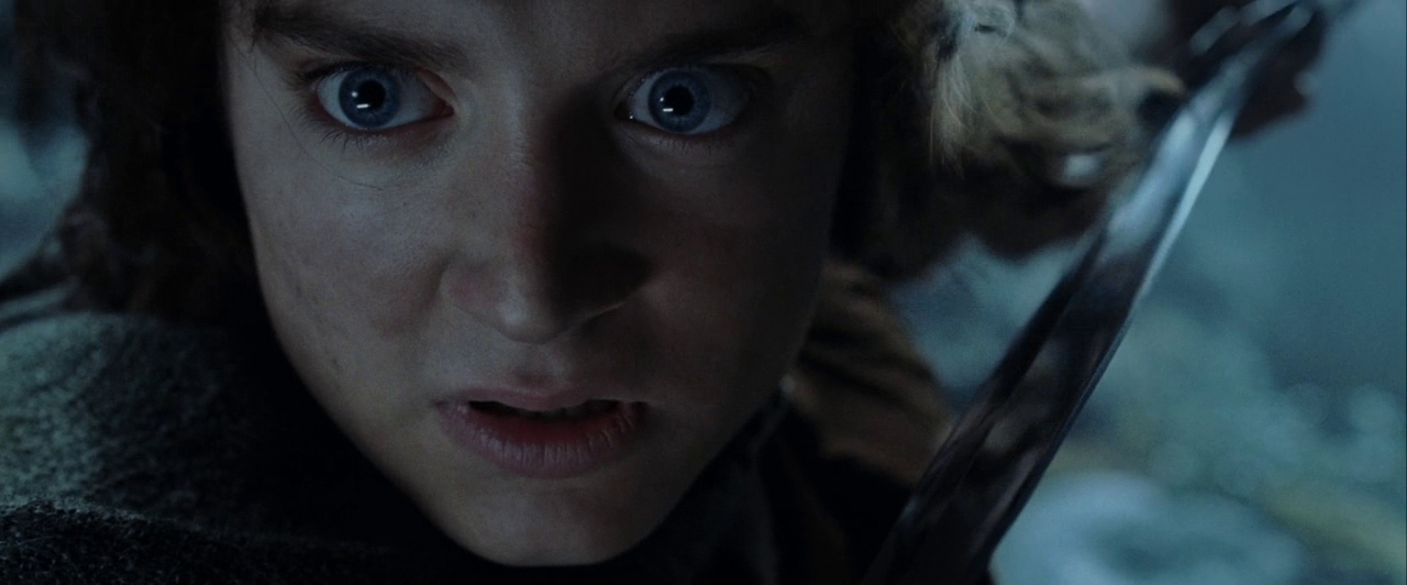 A dark outdoor environment at night with a hint of mist or fog. A young male with large blue eyes stares directly at the viewer while holding a sword.