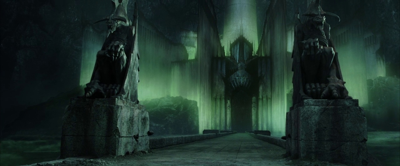 A massive stone fortress entrance features two demonic winged statues flanking a bridge. Glowing green mist obscures the base of the dark, towering architectural gate.