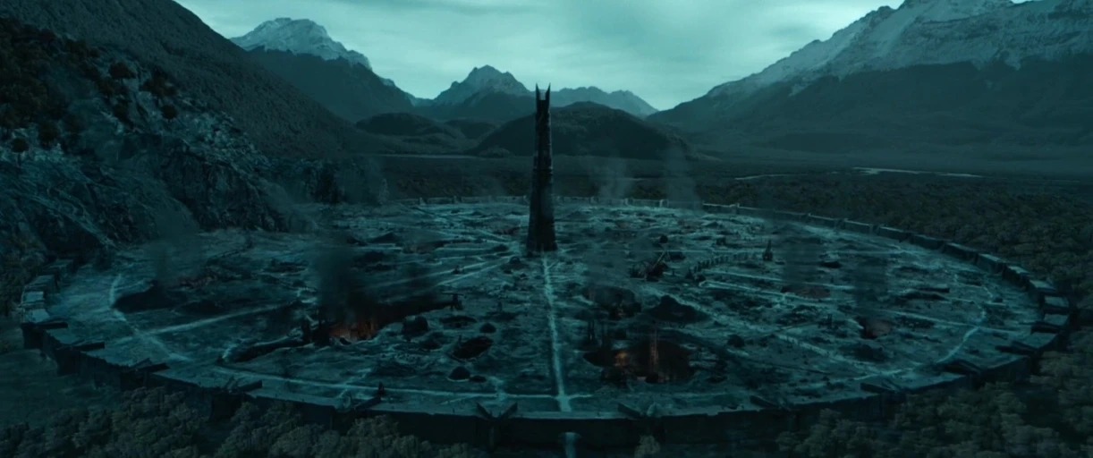A vast circular industrial fortress is embedded in a valley surrounded by snow-capped mountains. A tall obsidian spire sits at the center of the geometric trenches and pits.