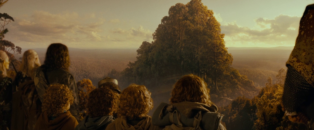 A group of travelers stands on a high mountain ridge looking out over a valley. A vast forest stretches toward the horizon under a soft golden sunset sky.