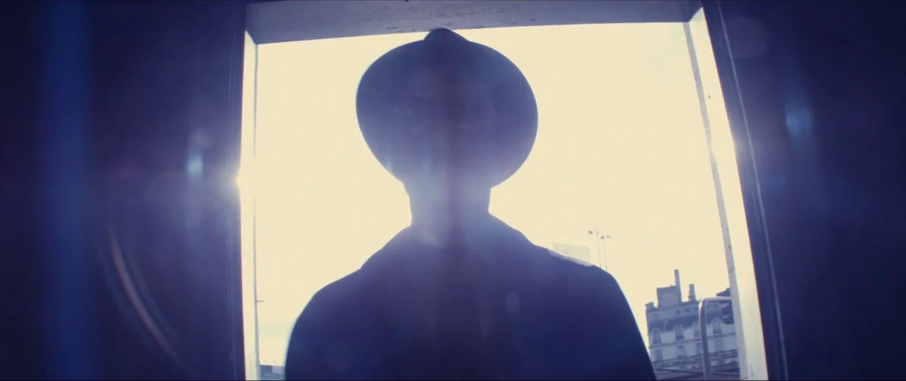 silhouette shots example from Neruda: A man stands in an exterior doorway framed against a bright daytime sky. The figure is captured in a dark silhou