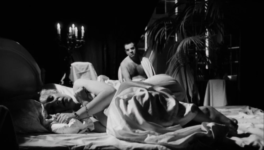 candlelight & firelight example from Veronika Voss: A dimly lit bedroom features a woman reclining on a bed under white linens. A man sits in the back