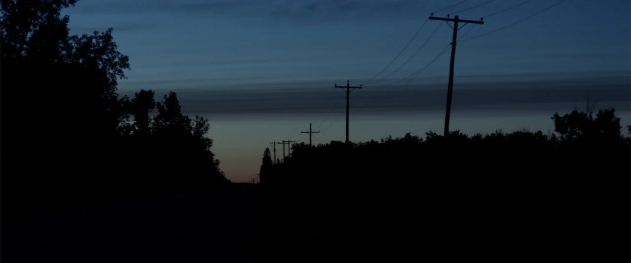 blue hour example from Radius: A rural road stretches into the distance beneath a twilight sky. Dark silhouettes of utility poles and dense trees line
