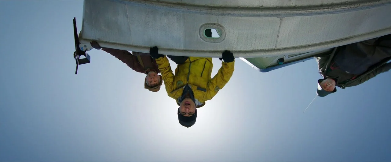 worm’s-eye shot example from Aquaman: Three men stand on a deck looking down at the camera from above. The sky is bright blue and the hull of a boat s