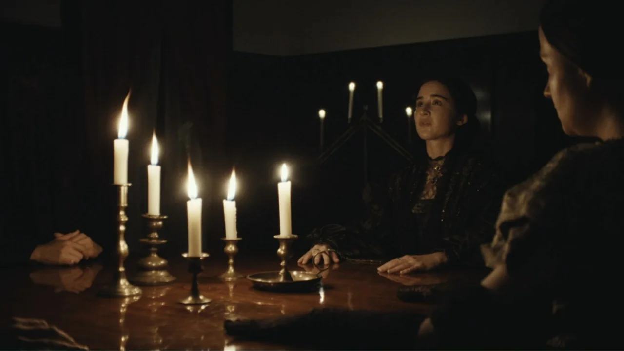 Demon in the White House (2021) movie still: medium — A dark dining room features a polished wooden table lit only by several candles. A woman sits…