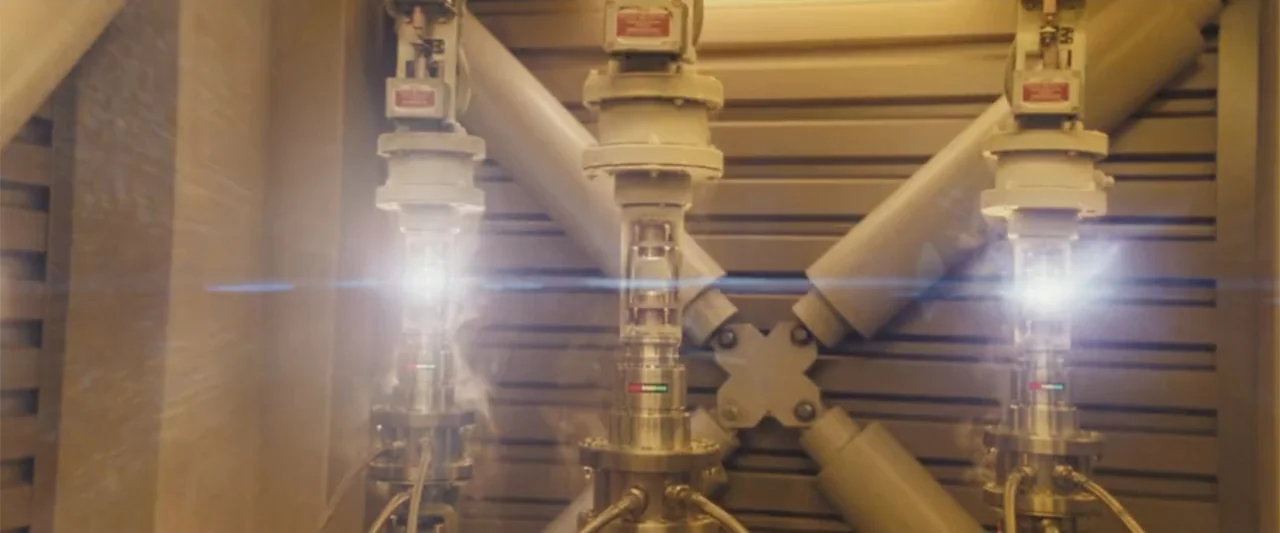 Angels & Demons (2009) movie still: medium — A close view of three metallic industrial pipes mounted against a reinforced steel wall. The glowing…