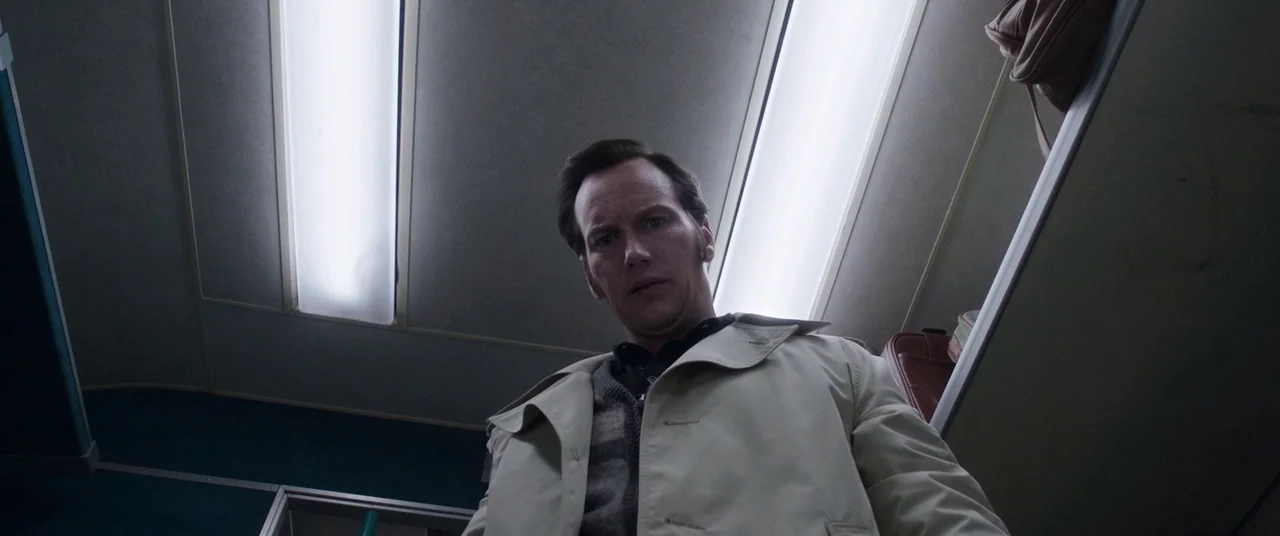 The Conjuring 2 (2016) movie still: medium — The interior of a commuter train carriage features overhead fluorescent light panels and luggage racks.…