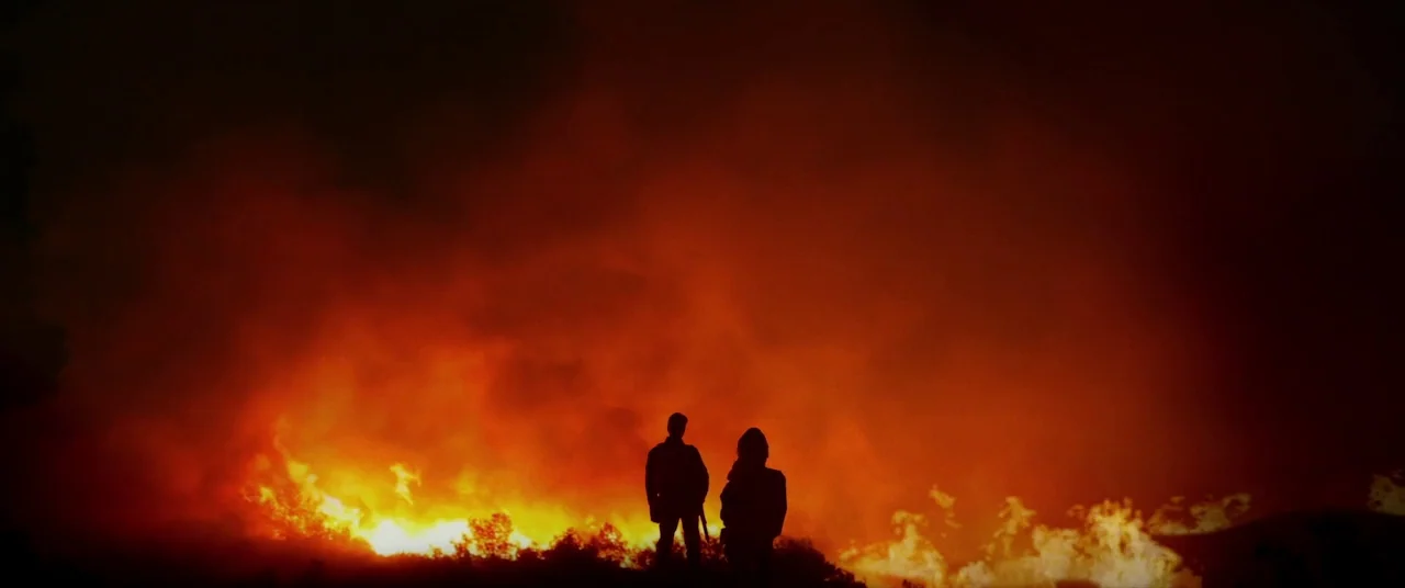 The Man Who Killed Hitler and Then the Bigfoot (2018) movie still: wide — A vast, dark outdoor area is engulfed in flames across the horizon. Two…