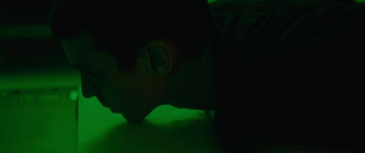 BPM (Beats Per Minute) (2017) movie still: closeup — A man is shown in profile against a dark background in a dim room. He leans close to an…
