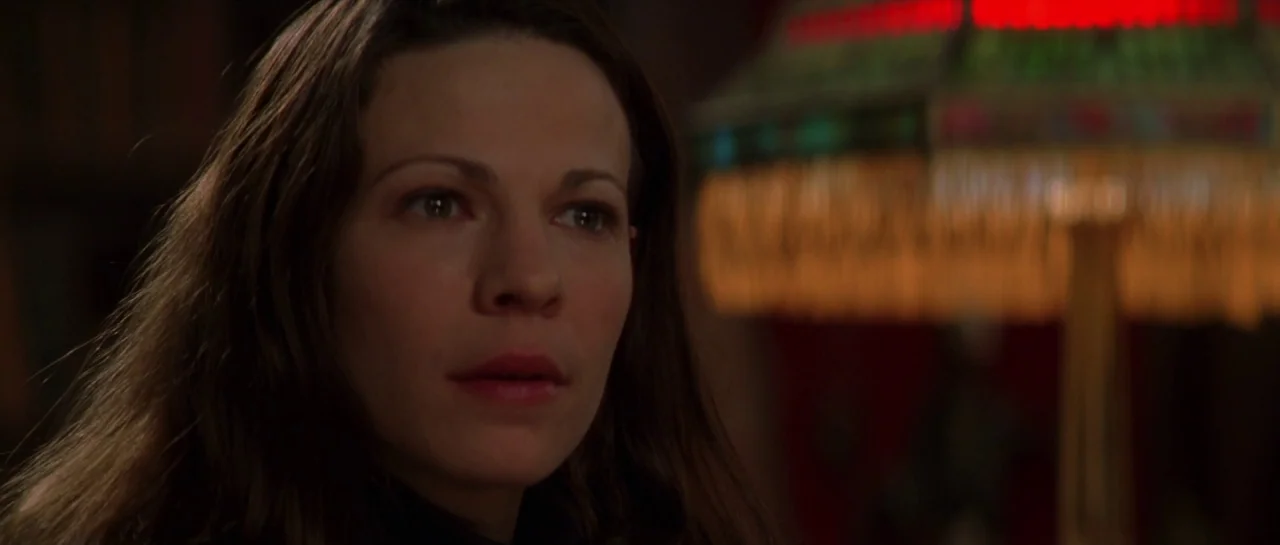 The Haunting (1999) movie still: closeup — A woman stands in a dimly lit room with dark surroundings and indistinct background. She focuses her gaze…