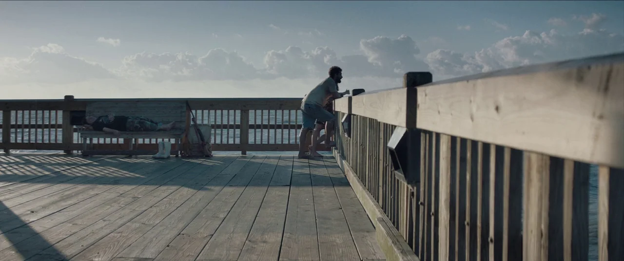 The Peanut Butter Falcon (2019) movie still: wide — A wooden pier extends over the ocean with a distant horizon under a cloudy sky. One man stands…