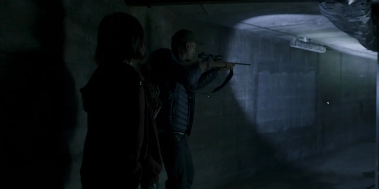 Demonic (2015) movie still: medium — A dark concrete tunnel has one narrow beam of light hitting a textured wall. A man aims a rifle with a scope…