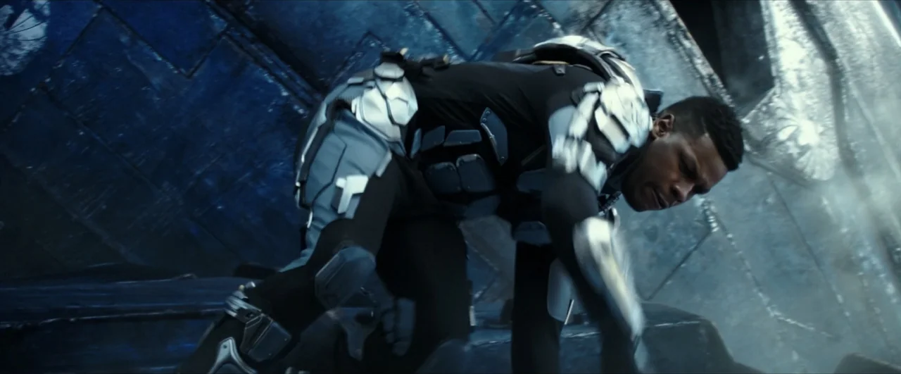dutch angle shots example from Pacific Rim: Uprising: A dark, angled futuristic passageway with blue textured walls and geometric surface panels. A ma