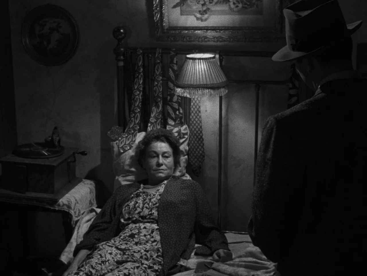 Pickup on South Street (1953) movie still: medium — A dim room contains an iron-framed bed with various ties hanging from the headboard. A woman…