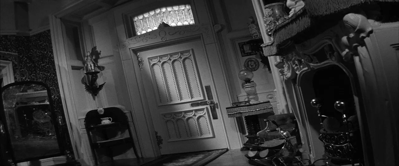 dutch angle shots example from The Haunting: An ornate parlor features a heavy front door and a decorative fireplace. Intricate dark wallpaper and per