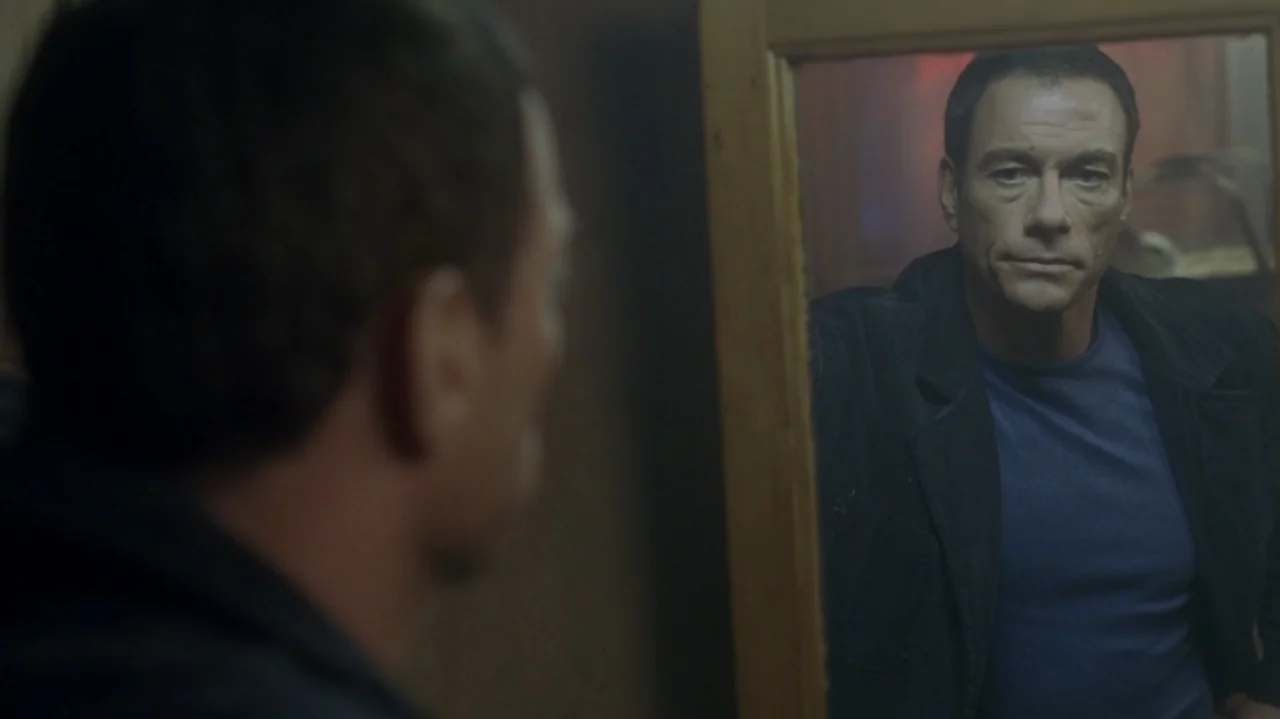 The Shepherd (2023) movie still: medium — A dimly lit room contains a person looking into a reflective glass surface. The subject examines his own…