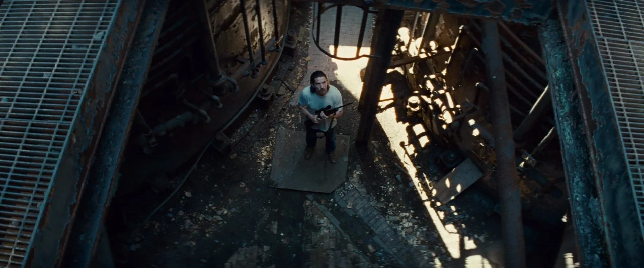Out of the Furnace (2013) movie still: wide — An industrial site features weathered metal tanks, pipes, and rusted floor gratings. A man stands…