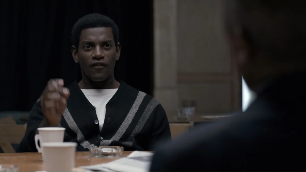 All the Way (2016) movie still: medium — A diner booth features a wooden table with paper cups and a glass ashtray. A young man sits in the booth…