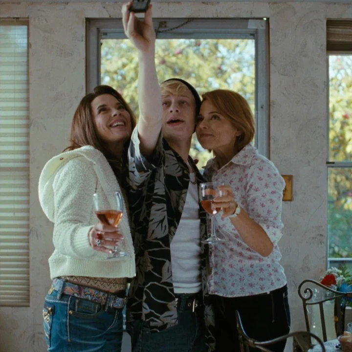 Mommy (2014) movie still: medium — A group of three people stands together indoors in a room with floral wallpaper. The trio holds wine glasses…