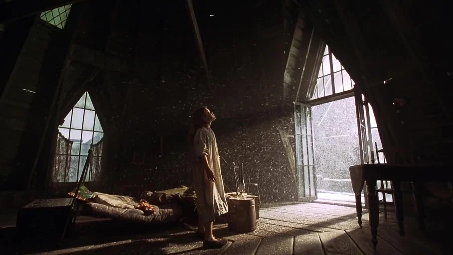 A Little Princess (1995) movie still: wide — An attic room with dark wooden walls and a pitched ceiling contains sparse furniture. A young girl in a…