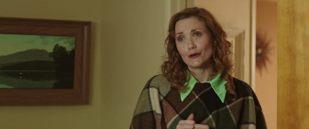 Southbound (2015) movie still: medium — A woman stands in a neutrally painted hallway next to a landscape painting. She is wearing a patterned…