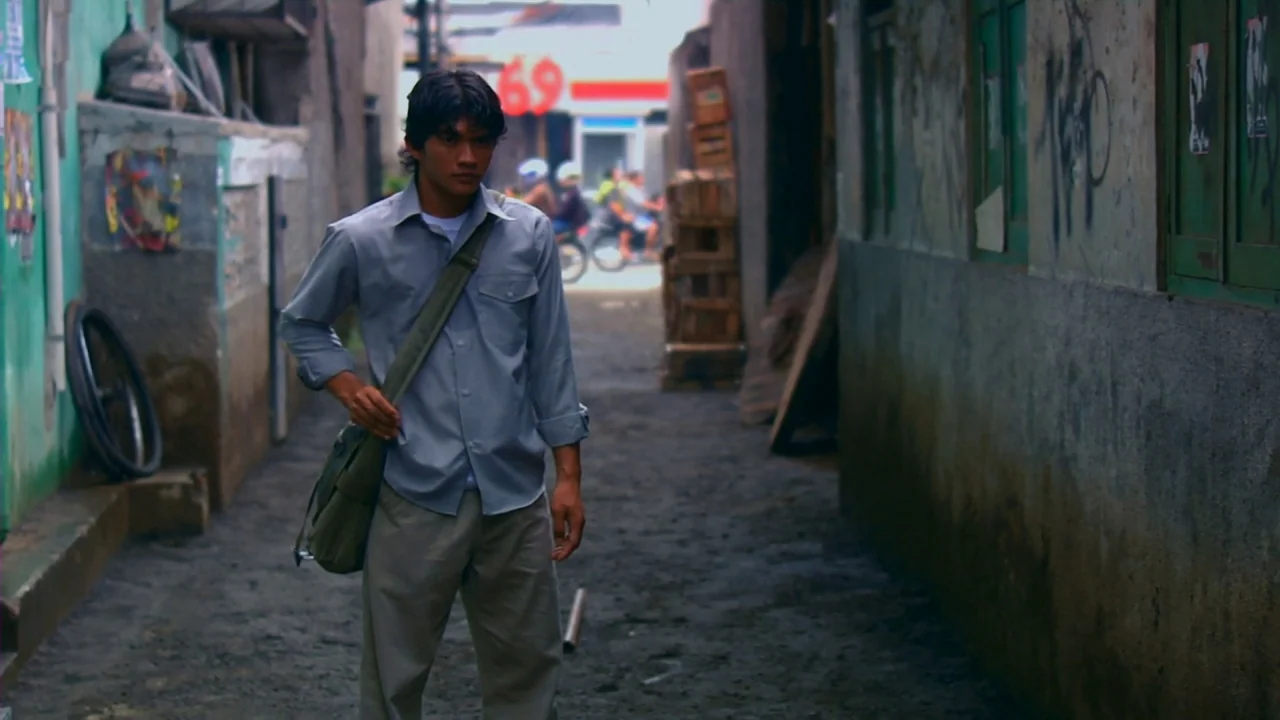 Merantau (2009) movie still: fullbody — A narrow, dirt-floored alleyway runs between weathered concrete walls with peeling teal and gray paint. A…