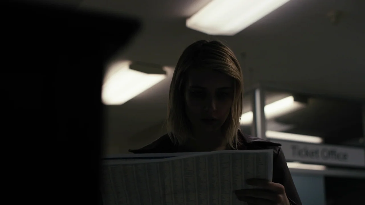 The Blackcoat’s Daughter (2015) movie still: medium — A dimly lit indoor transit area features fluorescent light fixtures and a ticket office sign.…