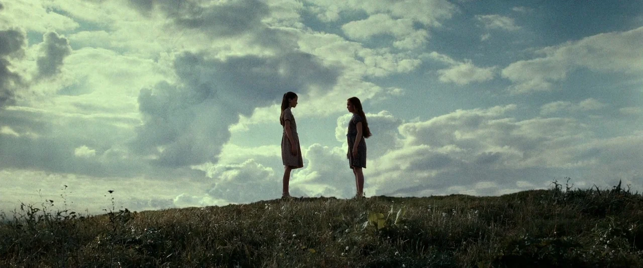 Harry Potter & The Deathly Hallows Part 2 (2011) movie still: wide — A grassy hilltop under a vast sky filled with heavy, layered clouds. Two young…