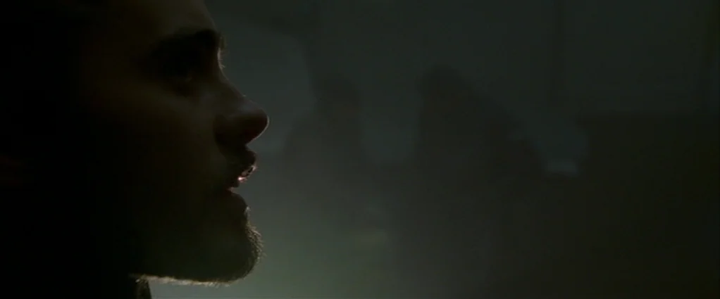 Panic Room (2002) movie still: closeup — A dark, nondescript interior space is shrouded in heavy shadow. A man is visible in profile, looking…
