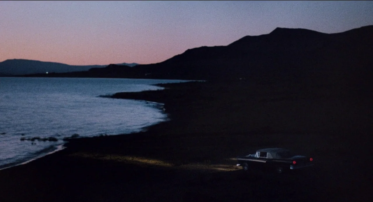 Desert Hearts (1985) movie still: wide — A dark, expansive lakeshore under a twilight sky with a mountain silhouette in distance. A vintage 1950s…