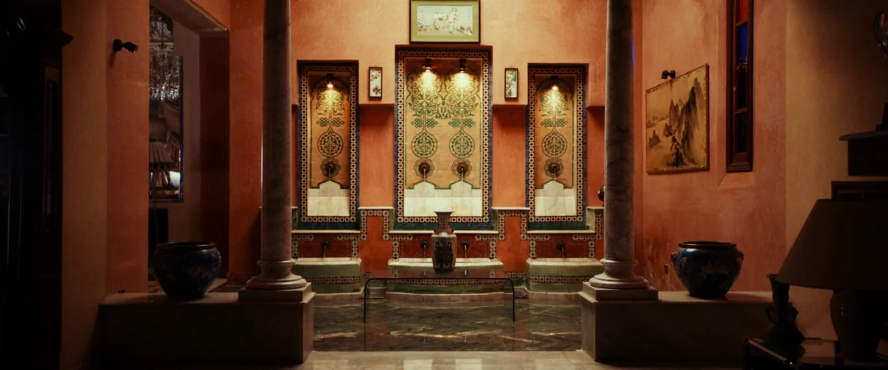 Animalia (2023) movie still: establishing — A terracotta-walled atrium features three recessed fountain niches framed by patterned ceramic tiles.…