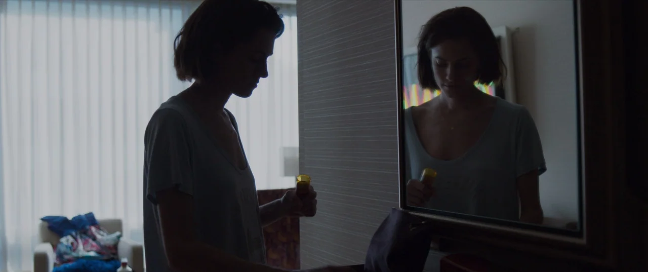 The Perfection (2018) movie still: medium — A hotel room with a window covered by white sheer curtains and patterned wallpaper. A woman stands in…