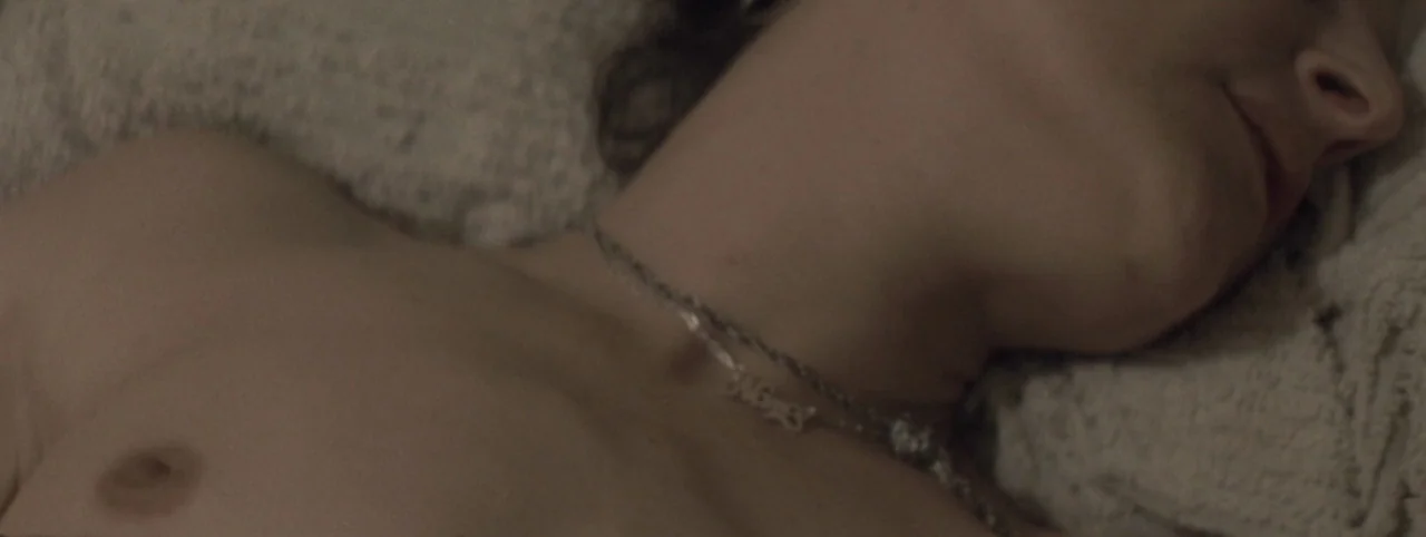 Post Mortem (2010) movie still: closeup — A close view of a person lying on textured fabric in an interior space. The subject is reclined with head…