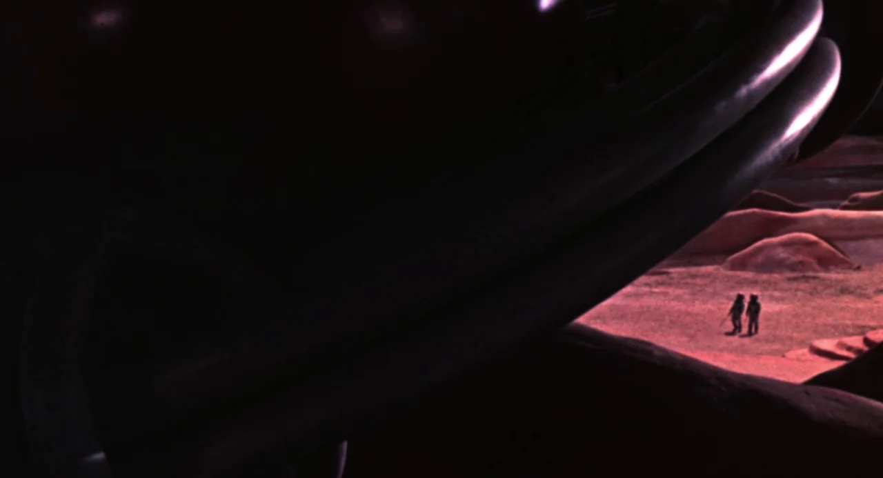 Queen of Blood (1966) movie still: wide — A dark alien landscape stretches out under a dim reddish sky. Two small astronauts walk across the rocky,…