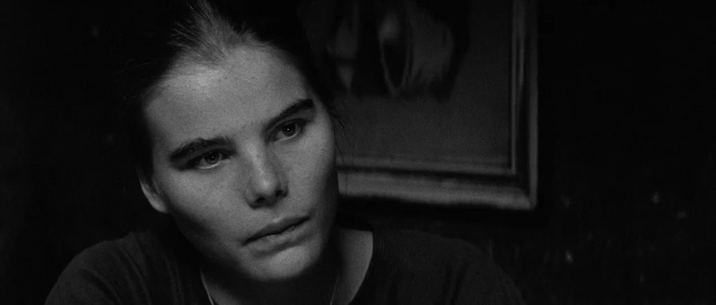 Manhattan (1979) movie still: closeup — An interior space with a dark wall behind the subject featuring a framed picture. A young woman with dark…