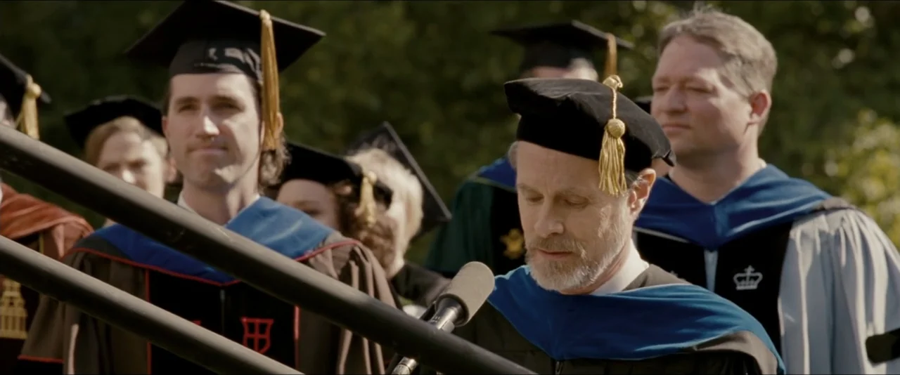 Into the Wild (2007) movie still: medium — A group of academics in formal graduation robes stand outdoors on a stage platform. A man with a grey…