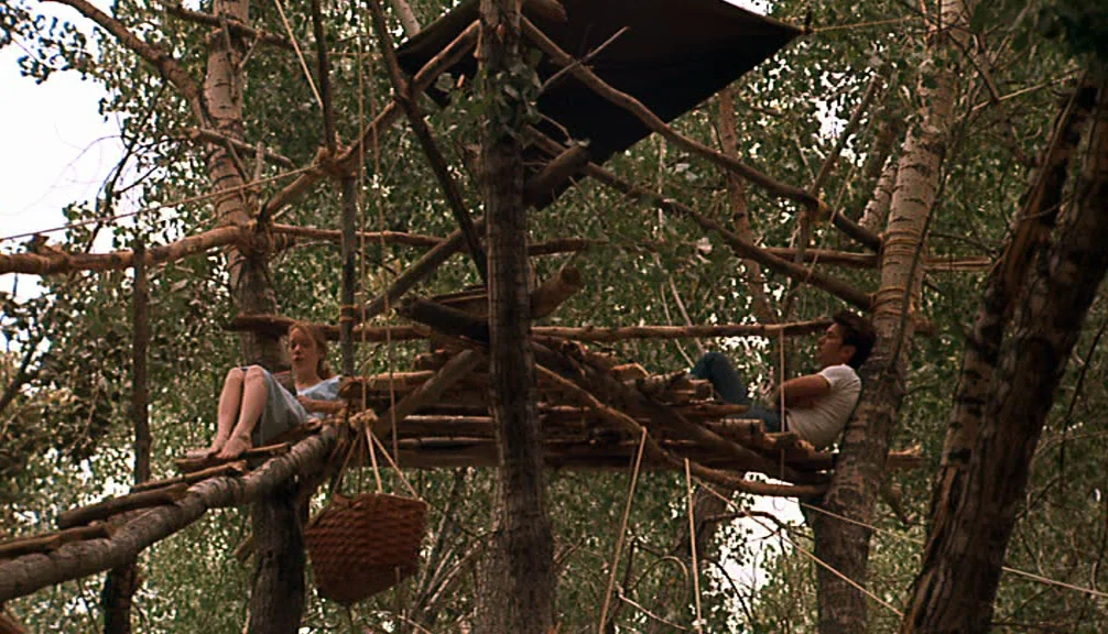 Badlands (1973) movie still: wide — A makeshift wooden platform built within the branches of tall birch trees. A man and a woman rest on the…